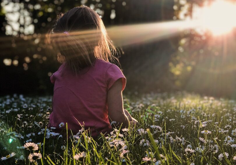 girl sitting on daisy flowerbed in forest