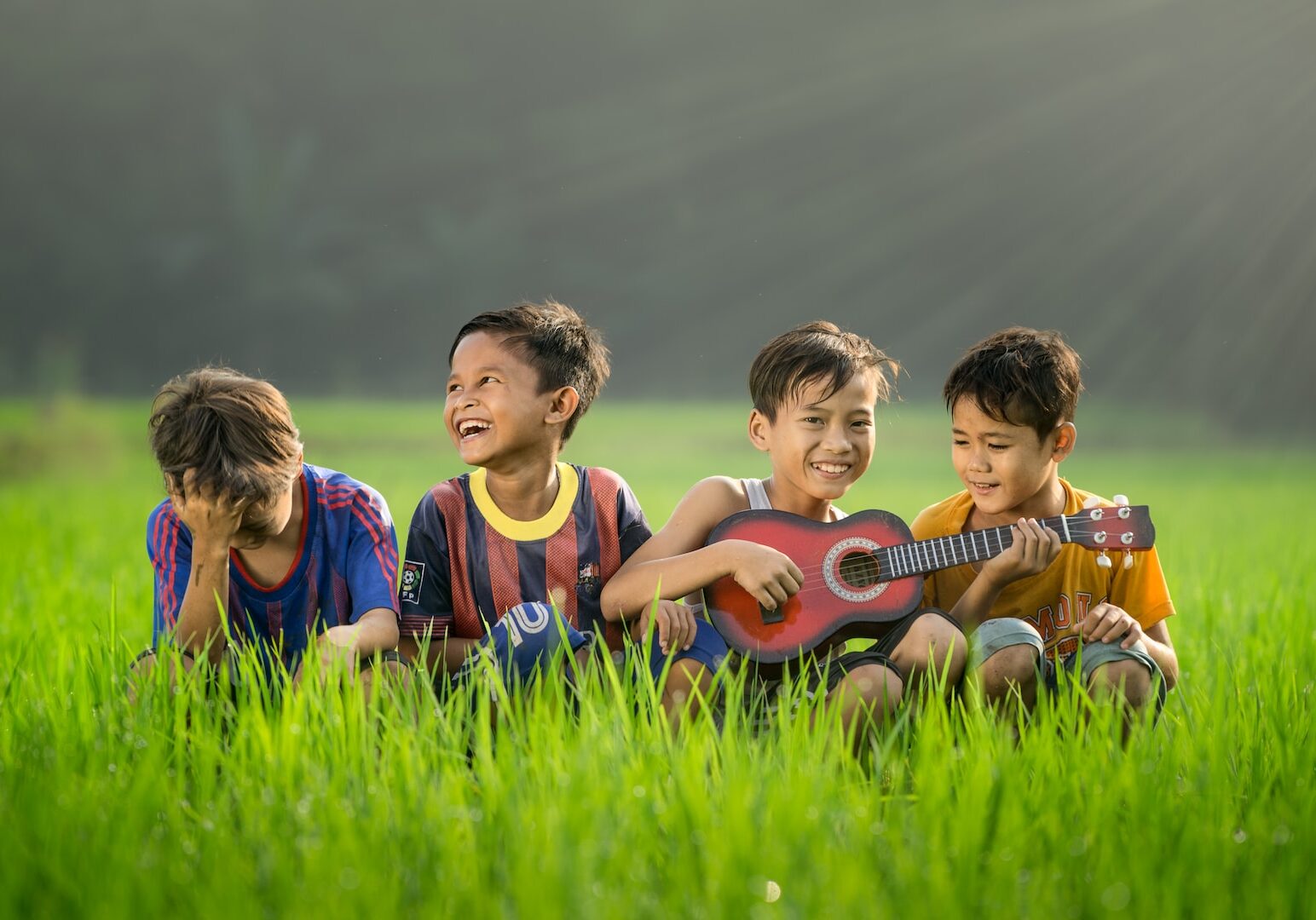 four boys laughing and sitting on grass during daytime